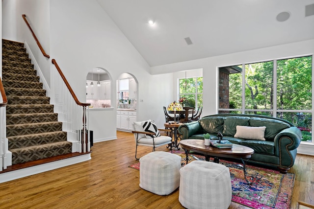living room with high vaulted ceiling, visible vents, stairs, and light wood finished floors