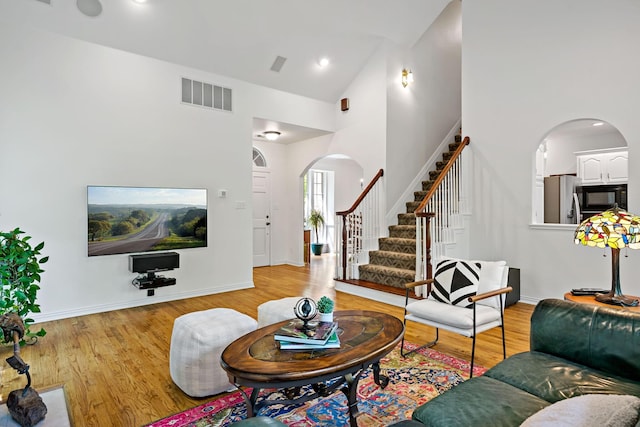 living room featuring wood finished floors, visible vents, arched walkways, and stairway