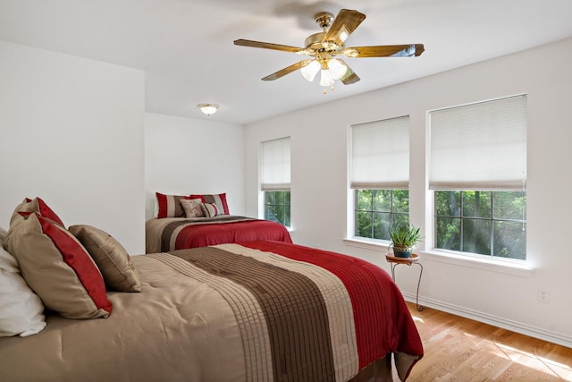 bedroom featuring baseboards, wood finished floors, ceiling fan, and multiple windows
