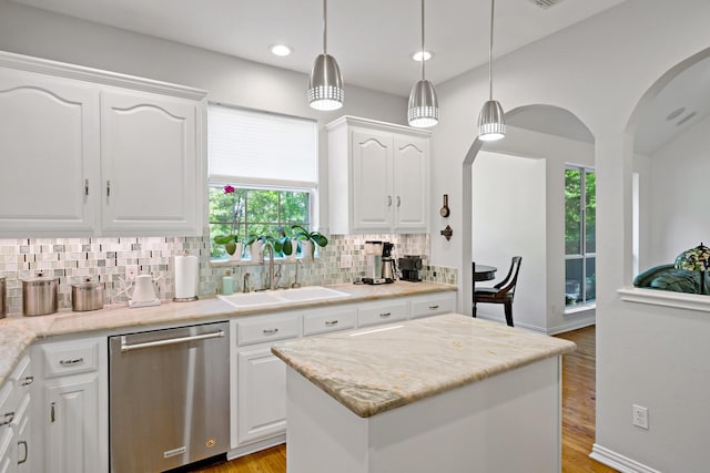 kitchen with stainless steel dishwasher, arched walkways, a sink, a wealth of natural light, and tasteful backsplash