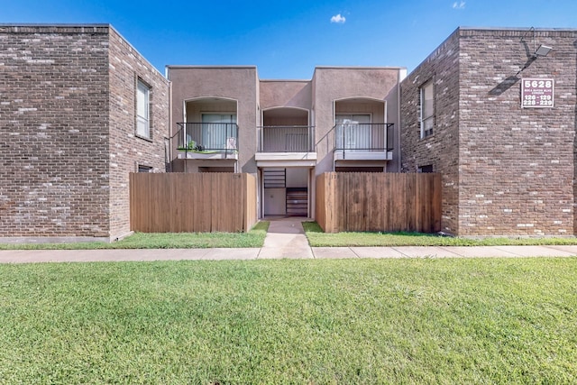 view of front of property featuring stucco siding, a front lawn, fence, and a balcony