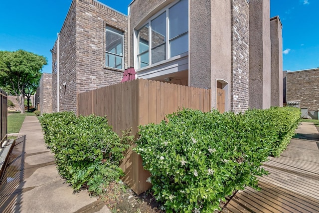 view of side of property with fence, brick siding, and stucco siding