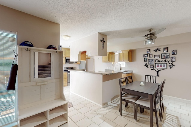 kitchen with stainless steel appliances, light brown cabinets, light tile patterned floors, a peninsula, and a textured ceiling