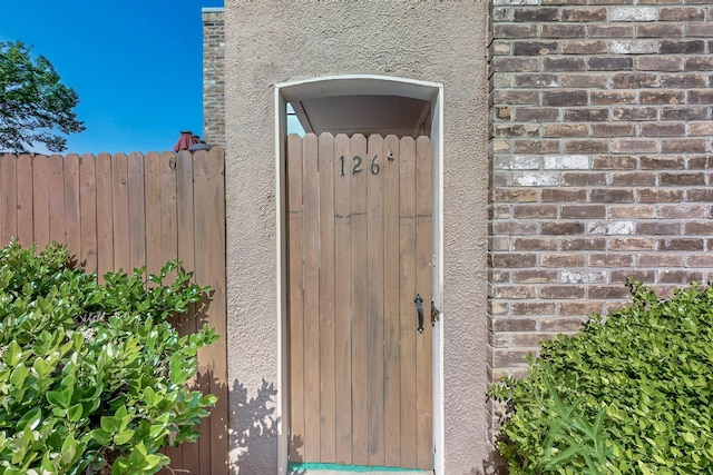 property entrance featuring stucco siding, brick siding, and fence