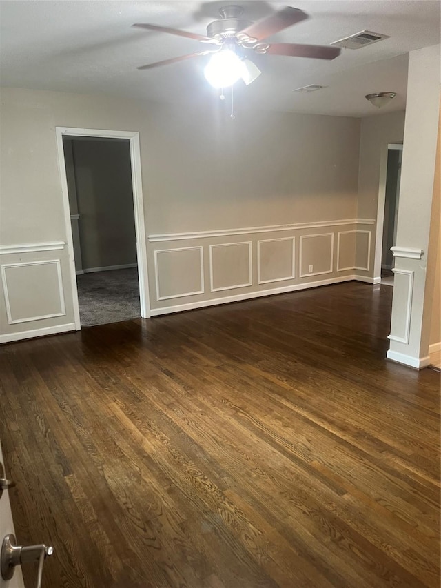 spare room featuring a decorative wall, a ceiling fan, dark wood-style flooring, and visible vents