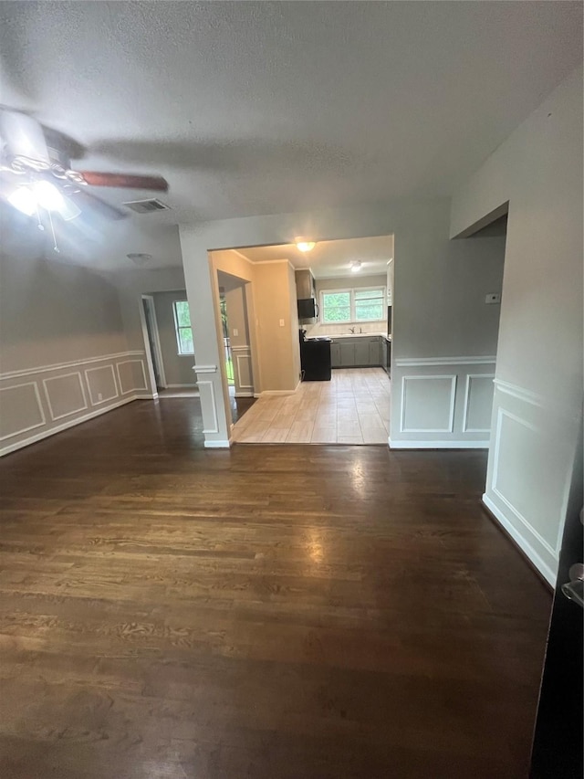 interior space featuring ceiling fan, a decorative wall, wood finished floors, and visible vents