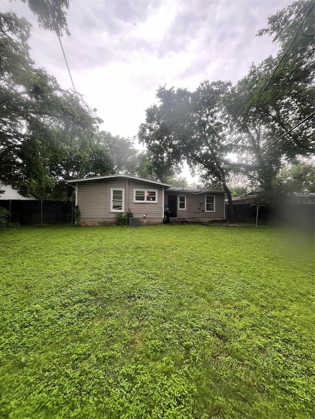 rear view of property featuring a lawn and fence
