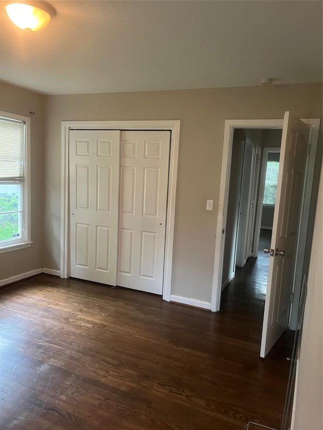 unfurnished bedroom featuring multiple windows, baseboards, and dark wood-style flooring