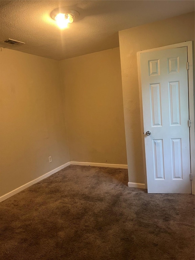 unfurnished room with baseboards, visible vents, dark carpet, and a textured ceiling