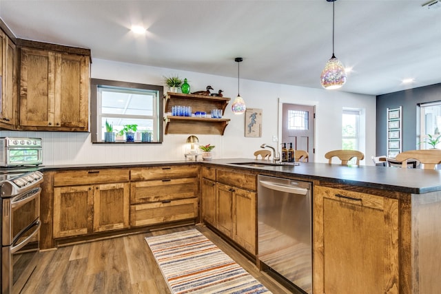 kitchen with a sink, a peninsula, brown cabinets, dark countertops, and appliances with stainless steel finishes
