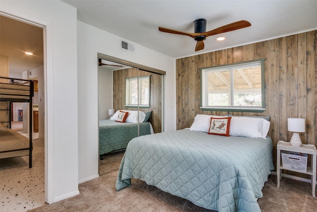 carpeted bedroom with wood walls, a closet, visible vents, ceiling fan, and baseboards
