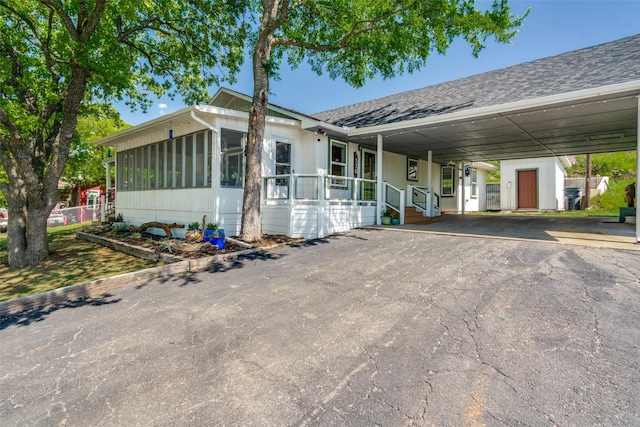 ranch-style house with an attached carport, a sunroom, a shingled roof, a shed, and driveway