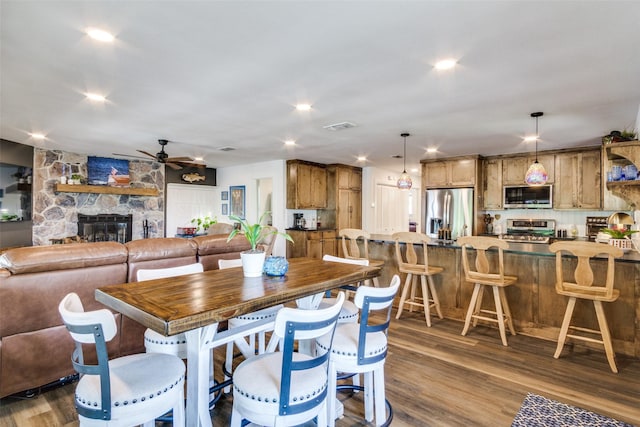 dining space featuring a fireplace, a ceiling fan, visible vents, and dark wood finished floors