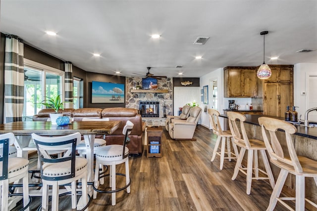 interior space with a ceiling fan, a stone fireplace, dark wood finished floors, and visible vents