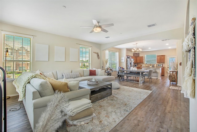 living area with arched walkways, baseboards, visible vents, ceiling fan with notable chandelier, and wood finished floors