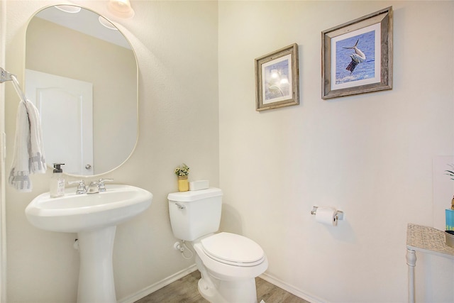 half bath with wood finished floors, baseboards, a sink, and toilet