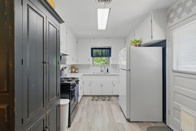 kitchen featuring black range with gas stovetop, a sink, freestanding refrigerator, light wood-style floors, and decorative backsplash