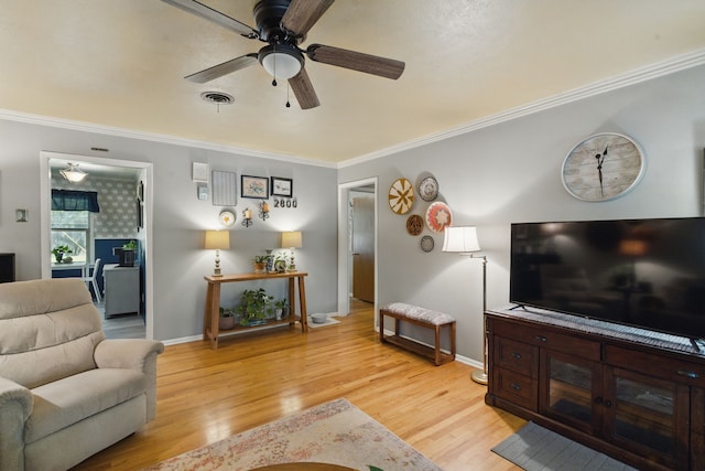 living area featuring light wood finished floors, visible vents, a ceiling fan, ornamental molding, and baseboards