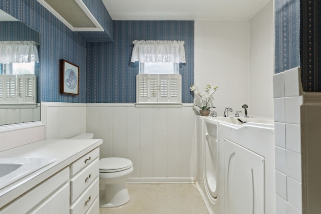 bathroom featuring wainscoting, wallpapered walls, vanity, and toilet