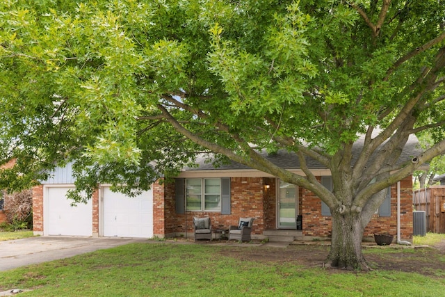 view of property hidden behind natural elements featuring central AC unit, driveway, fence, a front yard, and brick siding