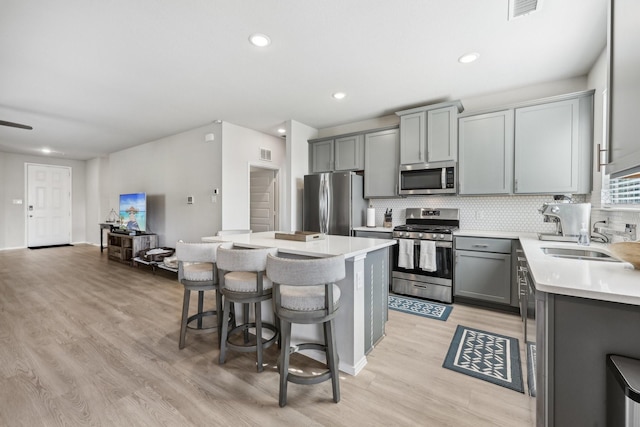 kitchen featuring a sink, stainless steel appliances, light wood-style flooring, gray cabinetry, and a kitchen island