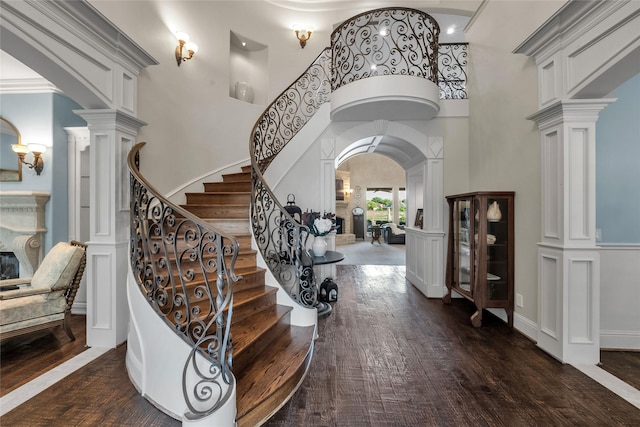 entryway with arched walkways, a towering ceiling, ornate columns, stairs, and dark wood-type flooring