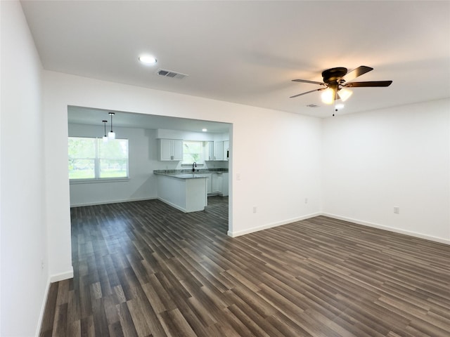 unfurnished living room with dark wood-style floors, visible vents, a sink, baseboards, and ceiling fan