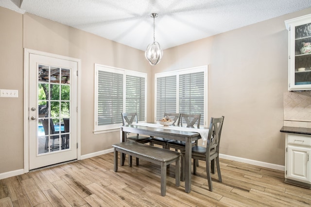 dining room with light wood-style flooring, baseboards, a textured ceiling, and a notable chandelier