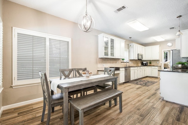 dining room with a textured ceiling, visible vents, light wood finished floors, and baseboards