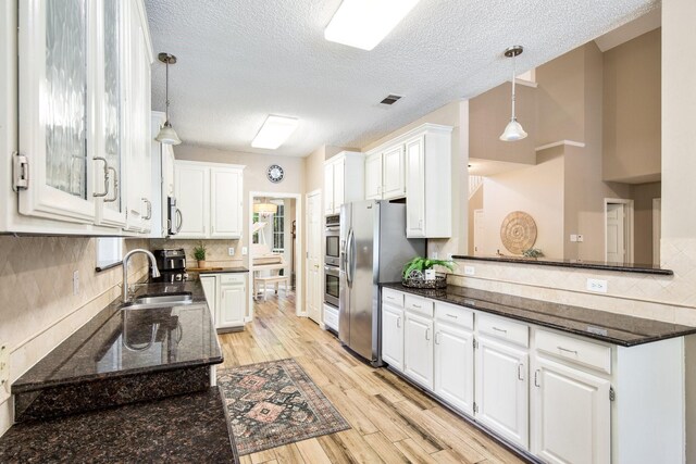 kitchen with a sink, a textured ceiling, light wood-style floors, white cabinets, and appliances with stainless steel finishes