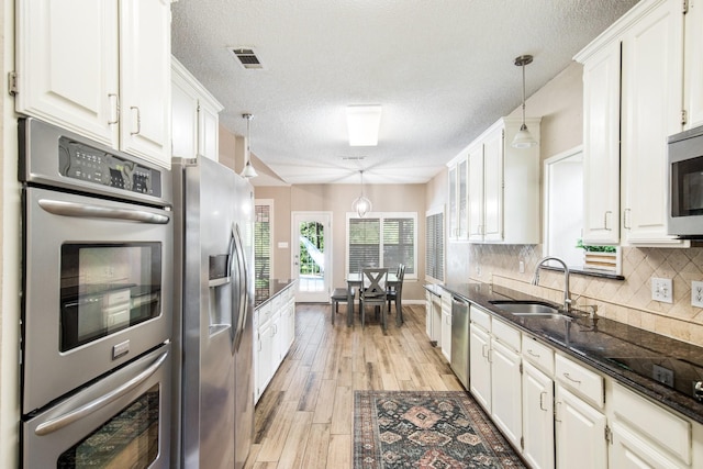 kitchen featuring white cabinets, stainless steel appliances, visible vents, a sink, and a textured ceiling