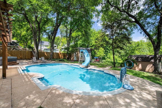 view of pool featuring a water slide, a fenced in pool, a fenced backyard, a patio area, and a storage unit