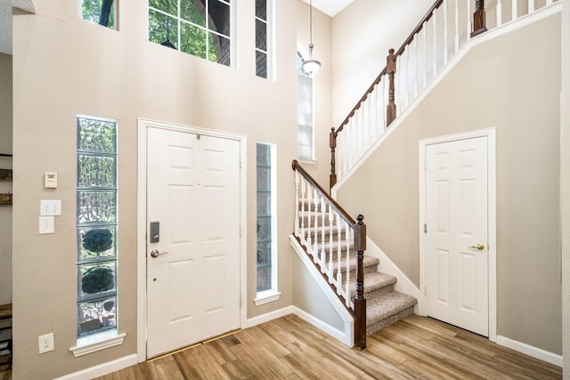 entrance foyer with stairway, a towering ceiling, wood finished floors, and baseboards