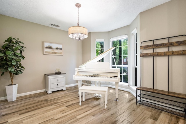 living area featuring light wood finished floors, a textured ceiling, baseboards, visible vents, and an inviting chandelier