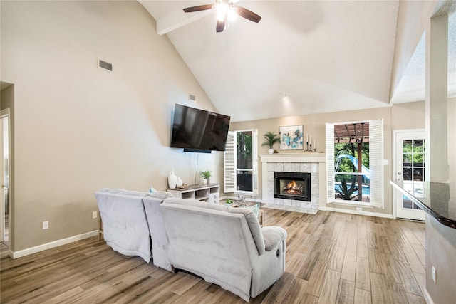 living area with a tile fireplace, wood finished floors, high vaulted ceiling, and ceiling fan