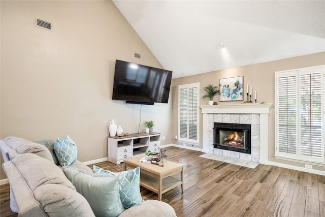 living room featuring a tile fireplace, wood finished floors, visible vents, baseboards, and high vaulted ceiling