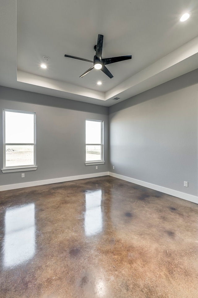 unfurnished room with ceiling fan, finished concrete flooring, a raised ceiling, baseboards, and recessed lighting