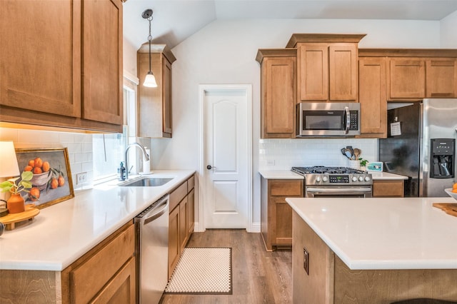 kitchen featuring stainless steel appliances, vaulted ceiling, a sink, light wood-type flooring, and tasteful backsplash