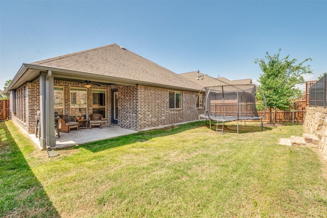 rear view of house with roof with shingles, brick siding, a patio area, and a trampoline