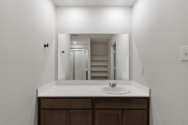 full bathroom featuring a textured wall, vanity, a stall shower, and visible vents