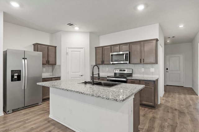 kitchen featuring tasteful backsplash, dark brown cabinets, a sink, light wood-type flooring, and appliances with stainless steel finishes