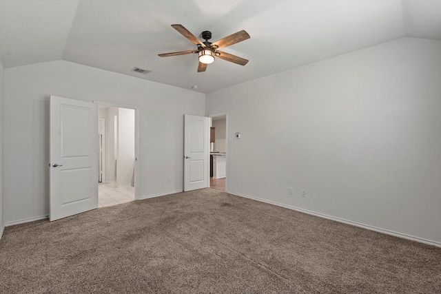 unfurnished bedroom featuring light colored carpet, vaulted ceiling, visible vents, and baseboards