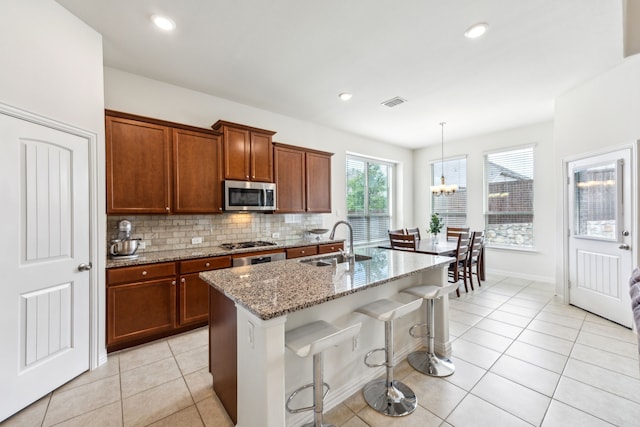 kitchen with light stone counters, a breakfast bar, gas cooktop, stainless steel microwave, and a sink