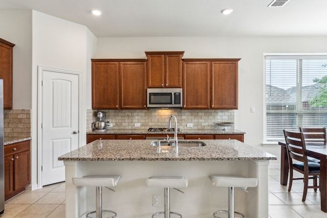 kitchen with light tile patterned floors, stainless steel microwave, a sink, light stone countertops, and a kitchen bar