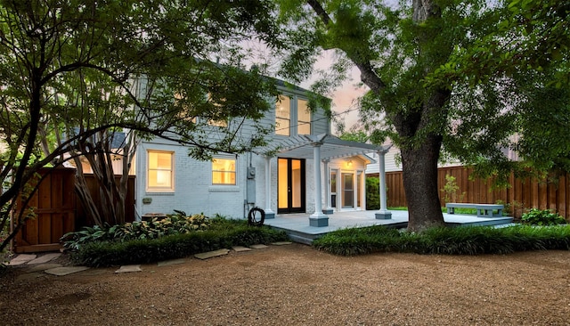 back of property at dusk with brick siding, fence, a patio area, and a pergola