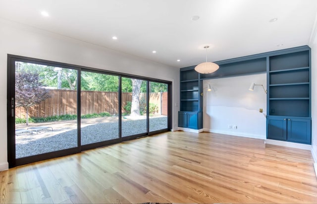 unfurnished living room featuring recessed lighting, ornamental molding, light wood-type flooring, and built in shelves