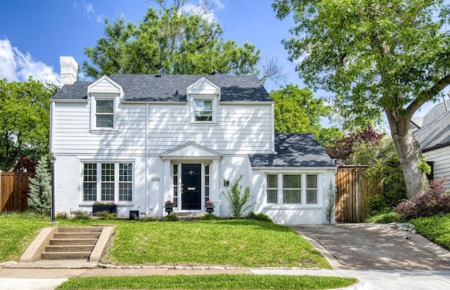 view of front of house featuring fence, a chimney, a shingled roof, and a front yard