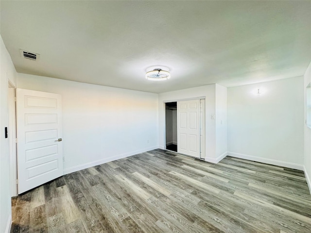 unfurnished bedroom with a closet, wood finished floors, visible vents, and baseboards