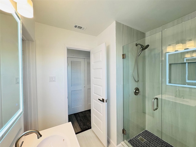 full bathroom featuring wood finished floors, visible vents, a sink, and a shower stall