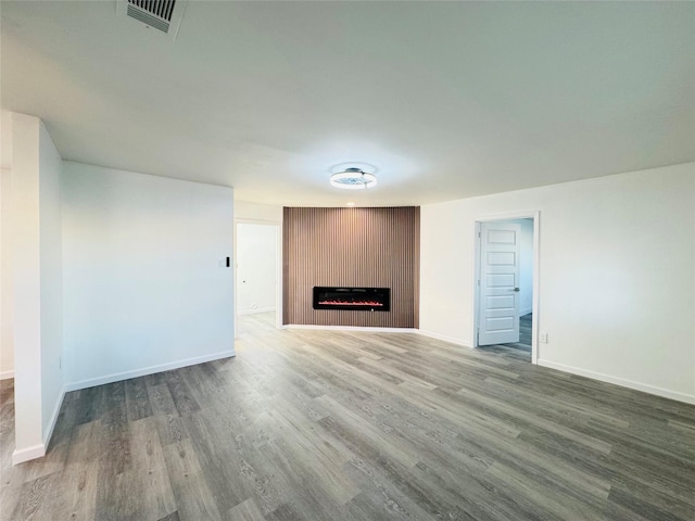 unfurnished living room with baseboards, wood finished floors, visible vents, and a fireplace